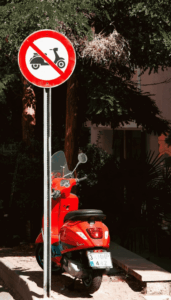 Verbodsbord voor scooters met een geparkeerde rode scooter erachter