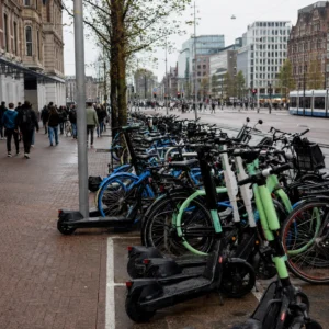 Volle deelvervoerhub met deelscooters en deelfietsen in een drukke Nederlandse binnenstad